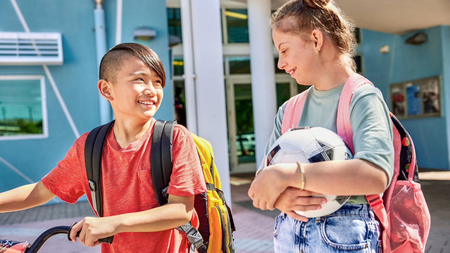 Two children leaving school with sports equipment